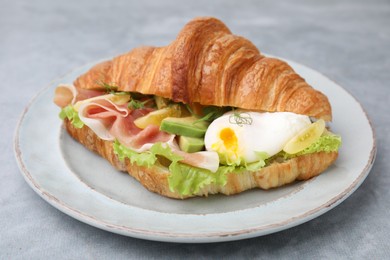 Photo of Delicious croissant with prosciutto, avocado and egg on grey table