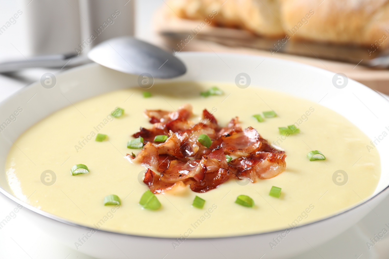 Photo of Tasty potato soup with bacon in bowl and spoon on table, closeup