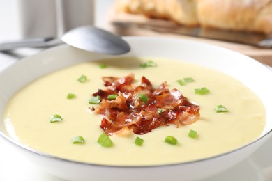 Tasty potato soup with bacon in bowl and spoon on table, closeup