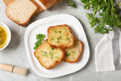 Photo of Slices of toasted bread with garlic and herb on light grey marble table, flat lay