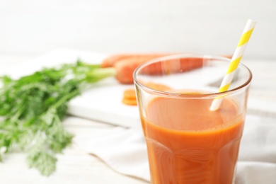 Glass of fresh carrot juice on white wooden table, space for text