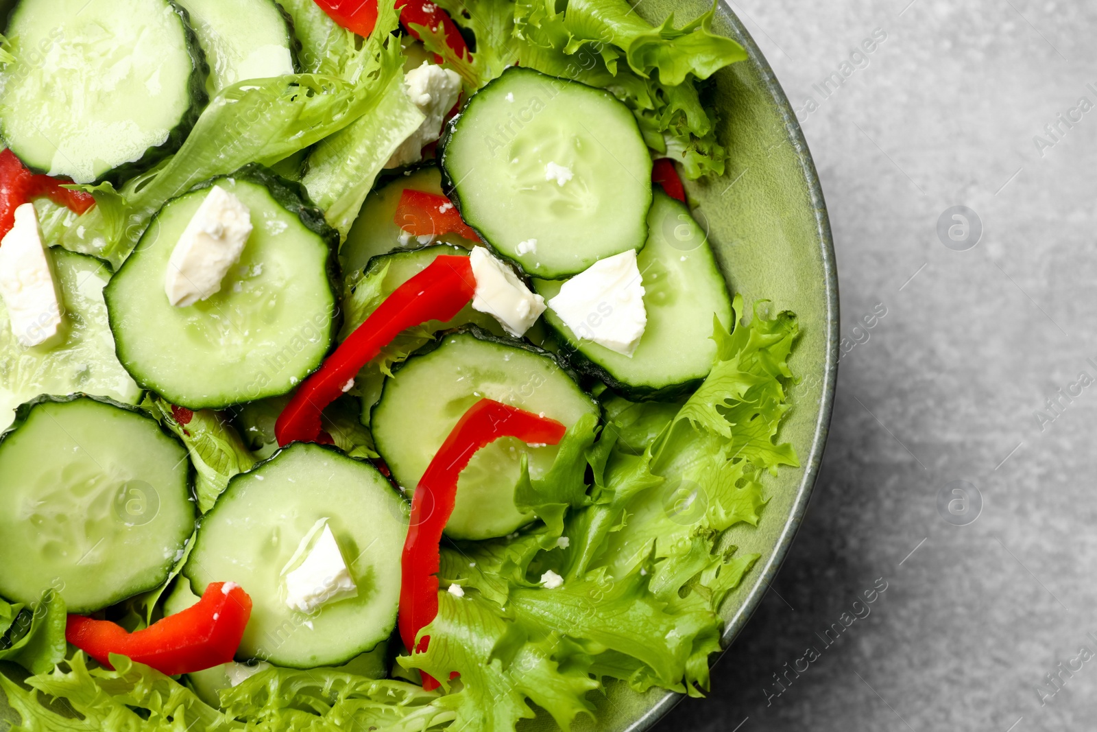 Photo of Delicious salad with cucumbers, red bell pepper and feta cheese in bowl on light grey table, closeup