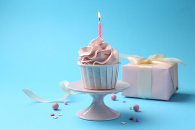 Delicious birthday cupcake with burning candle and sprinkles on light blue background, closeup