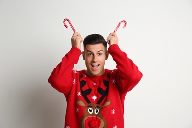 Funny man in Christmas sweater with candy canes on white background