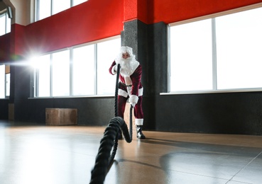 Young Santa Claus training with ropes in modern gym