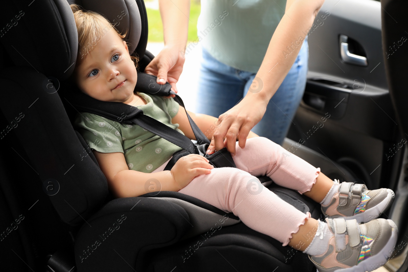 Photo of Mother fastening her daughter in child safety seat inside car