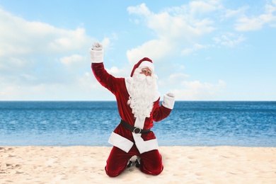 Image of Joyful Santa Claus on sandy beach near sea. Christmas vacation 