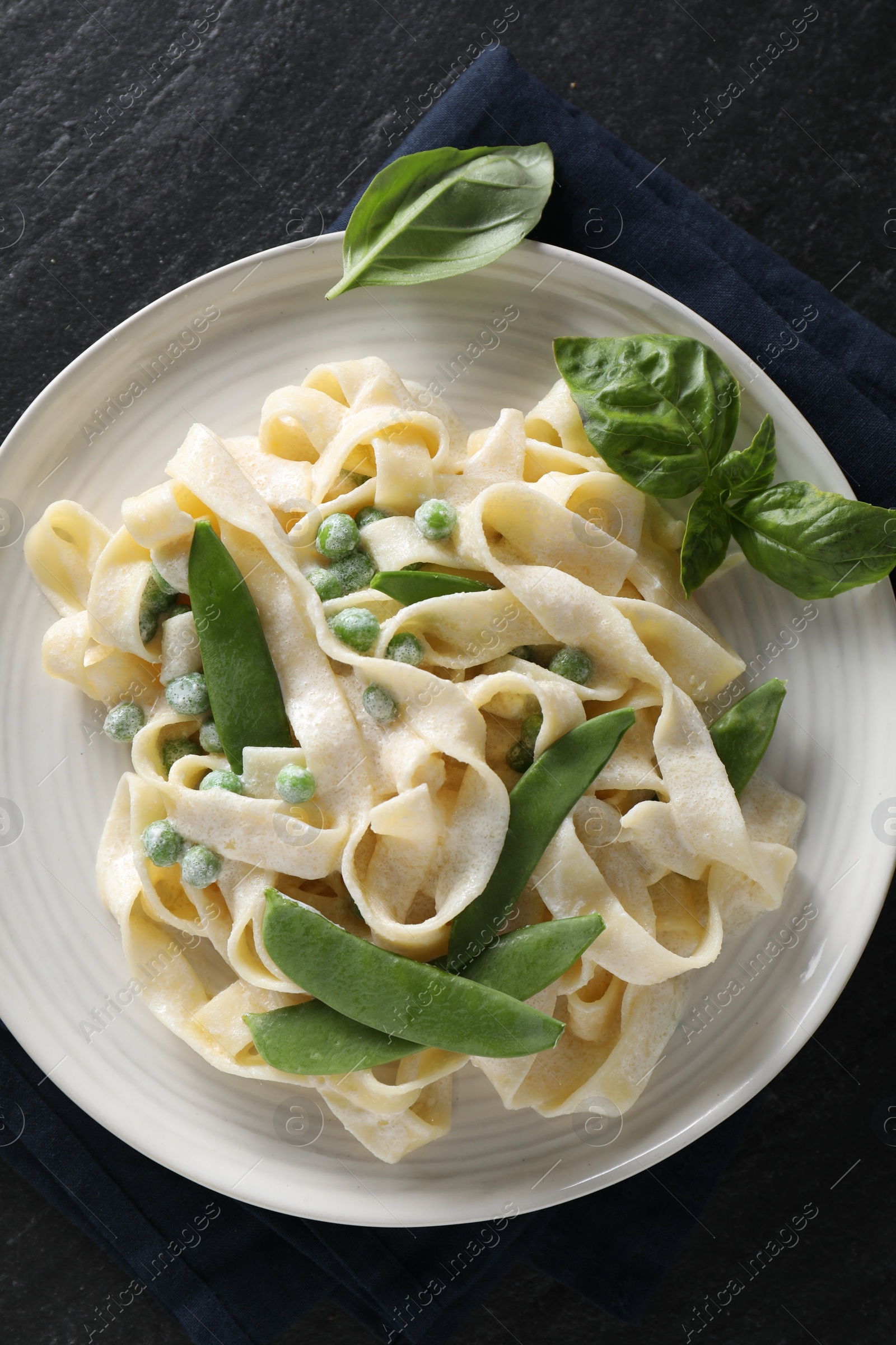 Photo of Delicious pasta with green peas and creamy sauce on black table, top view