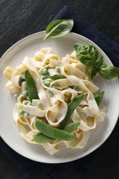 Photo of Delicious pasta with green peas and creamy sauce on black table, top view