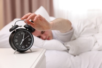 Man turning off alarm clock in bedroom, focus on hand. Space for text