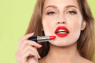 Young woman applying red lipstick on color background