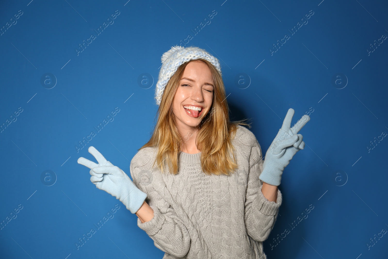 Image of Happy young woman wearing warm sweater, knitted hat and mittens on blue background 