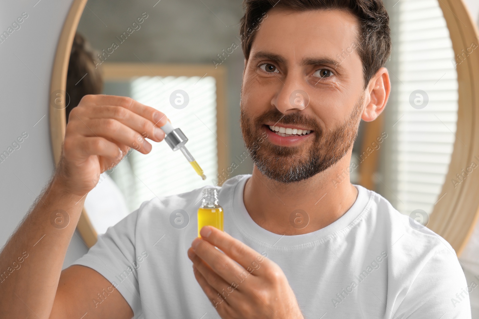 Photo of Smiling man with bottle of cosmetic serum indoors