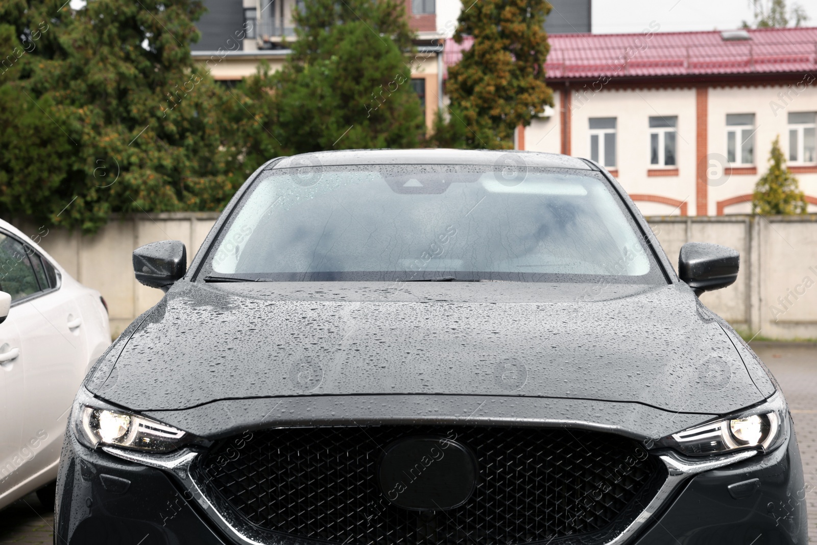 Photo of Black car with switched on headlights in drops of water parked outdoors