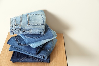 Photo of Stack of different jeans on table against light background. Space for text