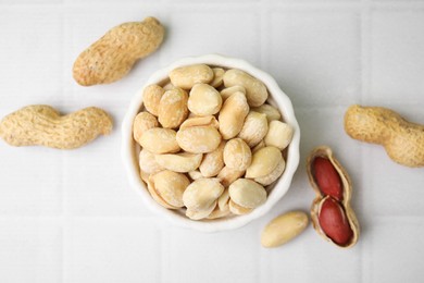 Photo of Fresh peeled peanuts in bowl on white tiled table, flat lay