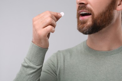 Man taking pill on light grey background, closeup