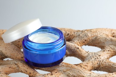 Open jar with moisturizing cream on wooden branch against light grey background, closeup