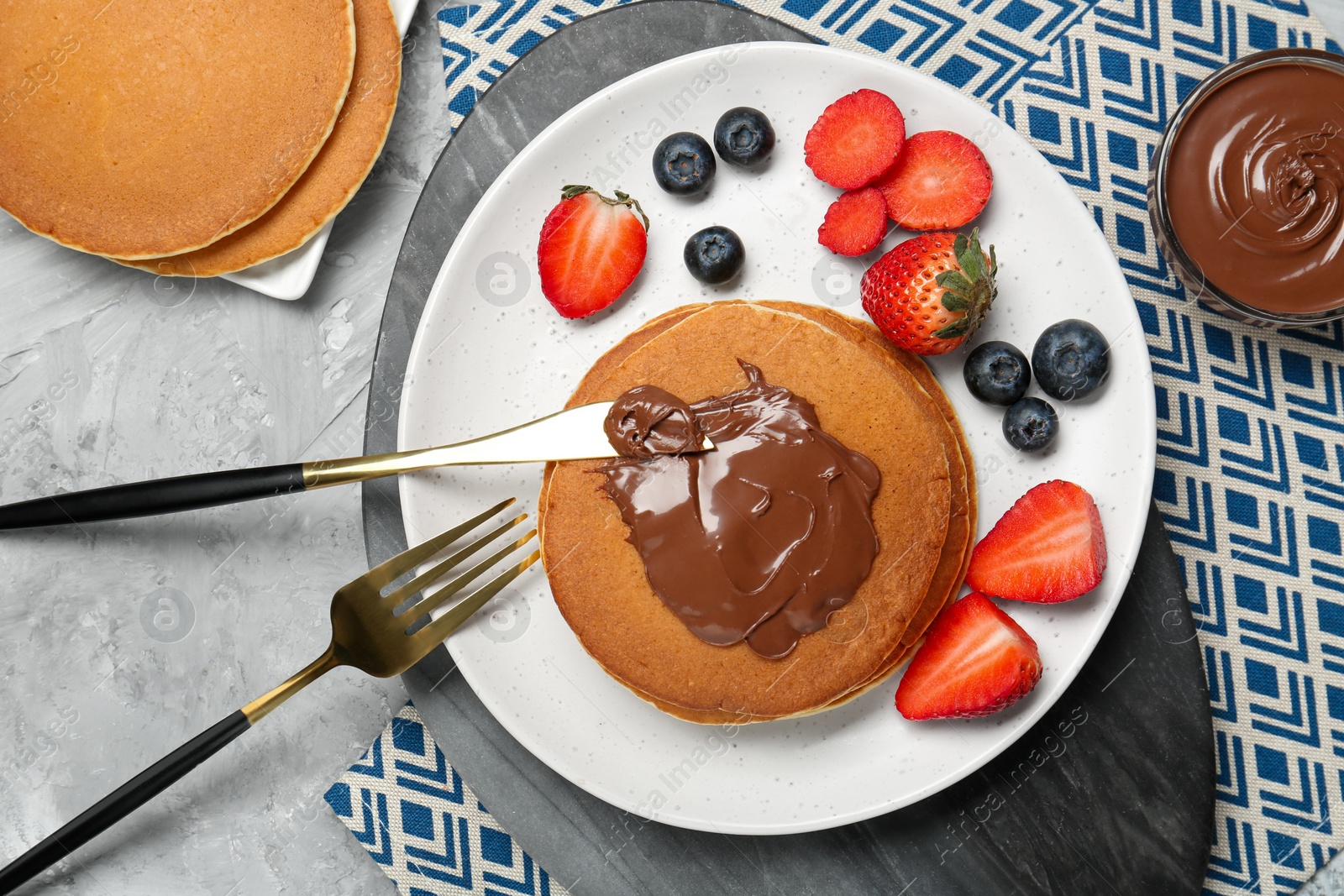 Photo of Tasty pancakes with chocolate paste and berries served on grey table, flat lay