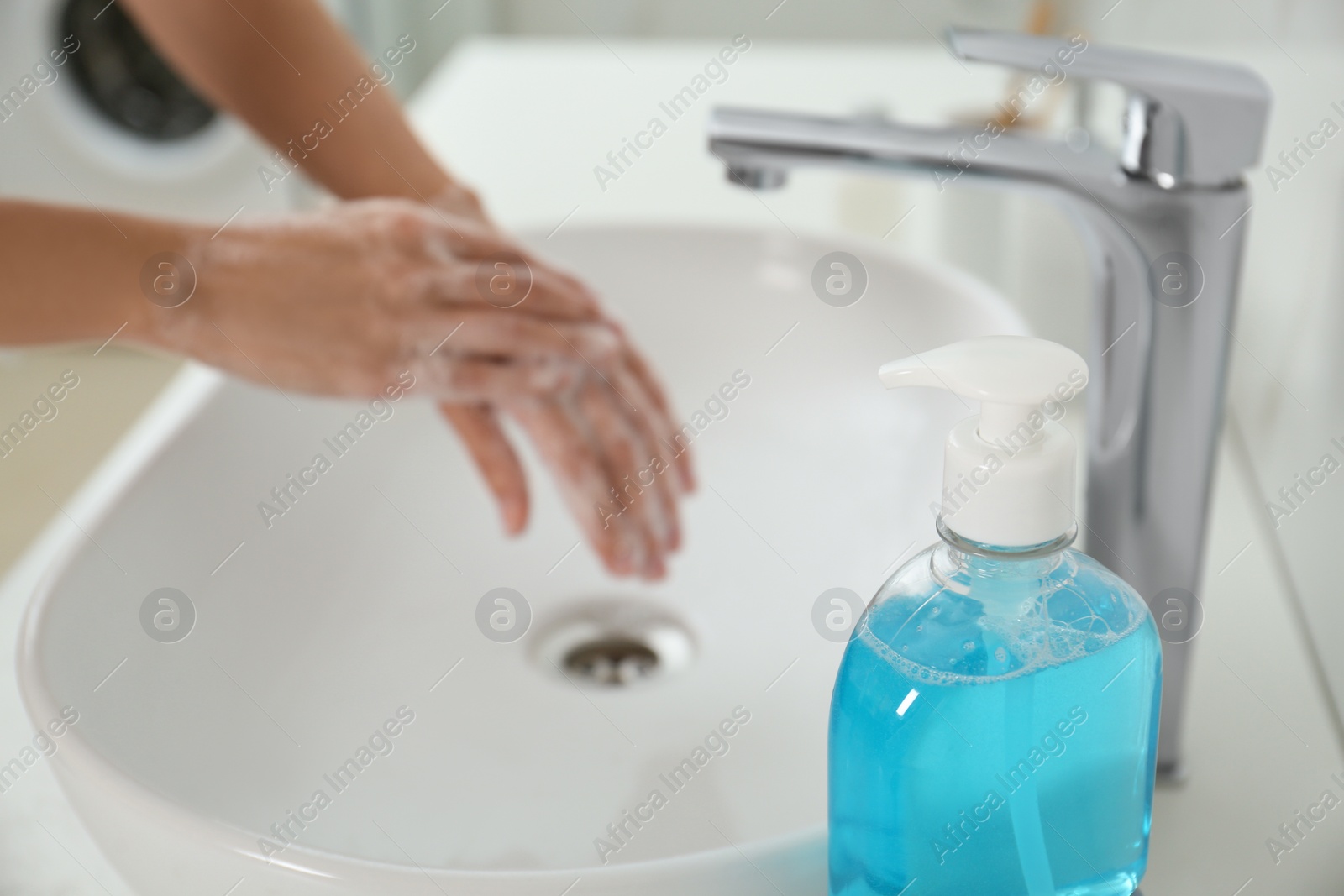 Photo of Bottle of antibacterial soap and blurred woman washing hands on background. Personal hygiene during COVID-19 pandemic