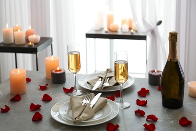 Romantic table setting with burning candles and rose petals indoors