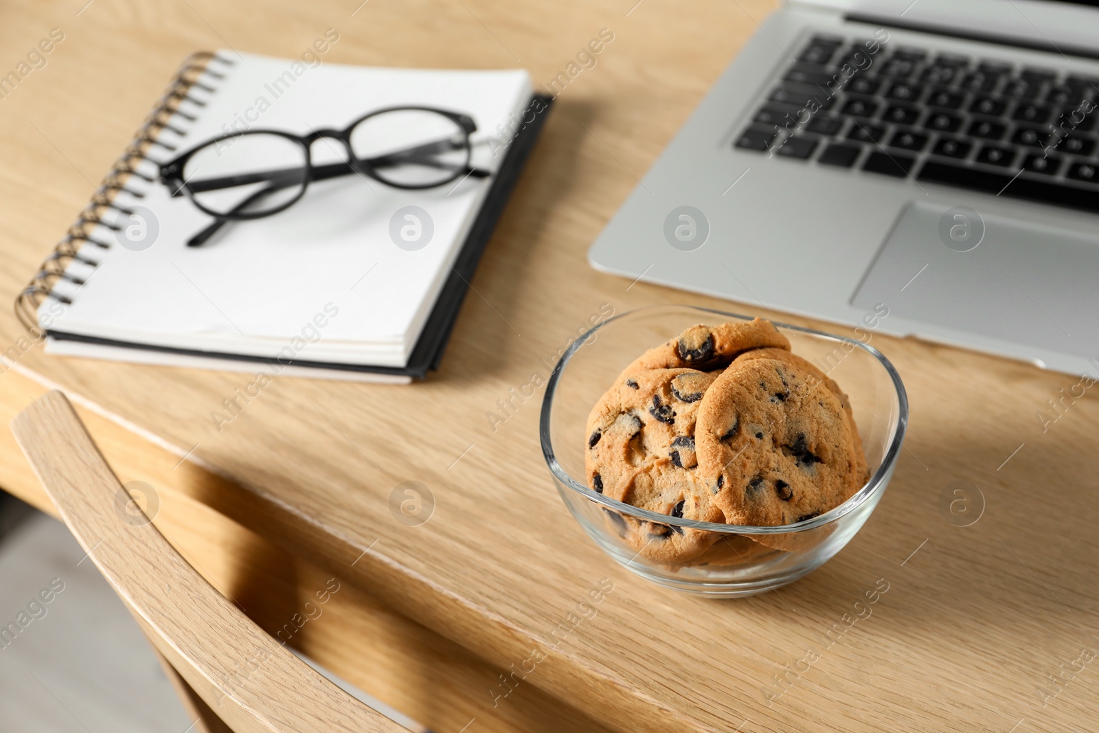 Photo of Chocolate chip cookies, notebook and laptop on wooden table at workplace