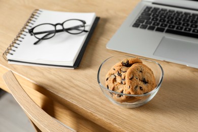 Photo of Chocolate chip cookies, notebook and laptop on wooden table at workplace