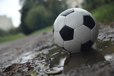 Leather soccer ball in puddle outdoors, space for text