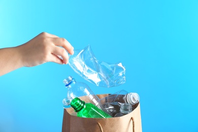 Photo of Woman putting used plastic bottle into paper bag on color background, closeup with space for text. Recycling problem