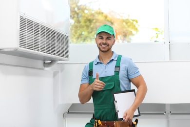 Professional technician with clipboard near modern air conditioner indoors