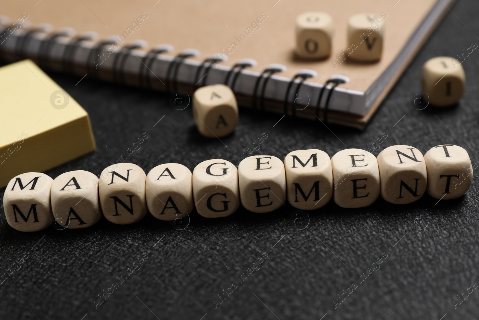 Photo of Word Management made of cubes near paper notes and notebook on black background, closeup