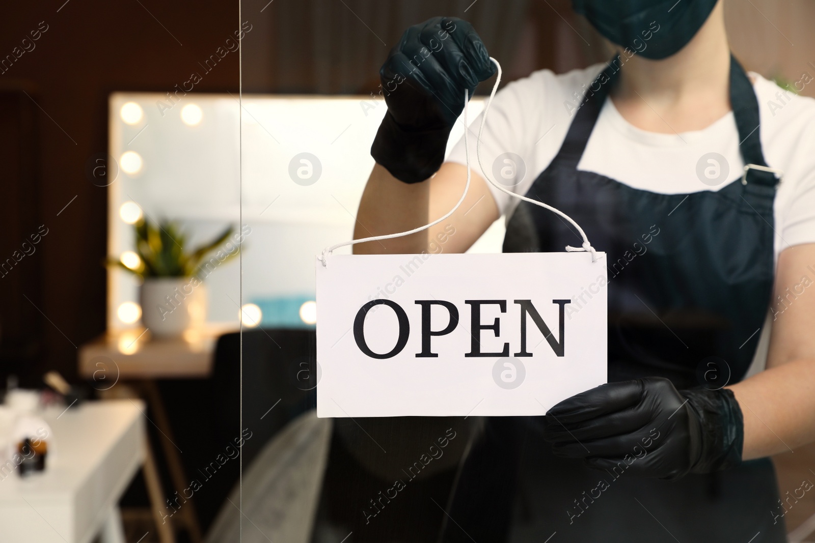 Photo of Woman hanging Open sign onto glass door in salon, closeup. Beauty services during Coronavirus quarantine