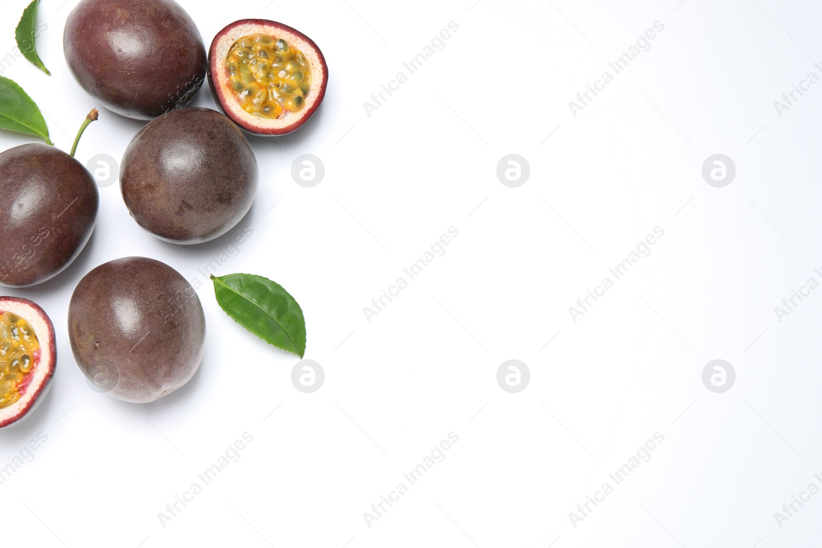 Photo of Fresh ripe passion fruits (maracuyas) with leaves on white background, flat lay. Space for text