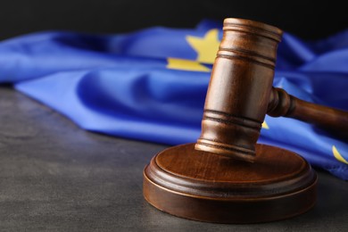 Photo of Wooden judge's gavel and flag of European Union on grey table, closeup. Space for text