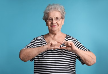 Photo of Elderly woman making heart with her hands on light blue background