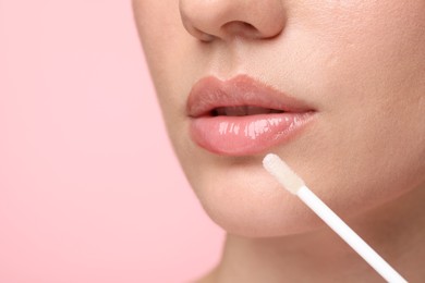 Photo of Woman applying lip gloss on pink background, closeup. Space for text