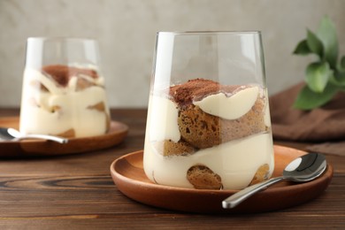 Photo of Delicious tiramisu in glasses and spoon on wooden table, closeup