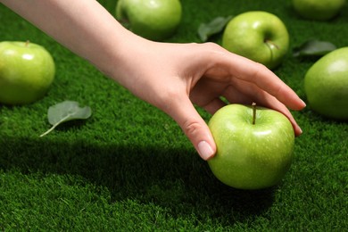 Photo of Woman picking ripe green apple up from grass, closeup