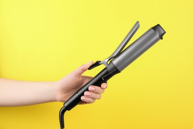 Photo of Hair styling appliance. Woman holding curling iron on yellow background, closeup