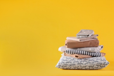 Photo of Stack of clean bed linen and pillow on yellow background. Space for text