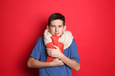 Photo of Sick teenage boy with hot water bottle on red background