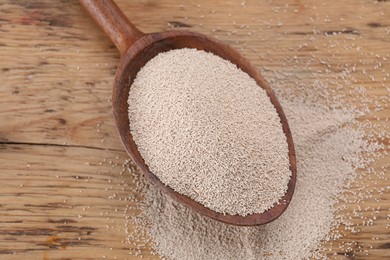 Photo of Spoon with active dry yeast on wooden table, above view