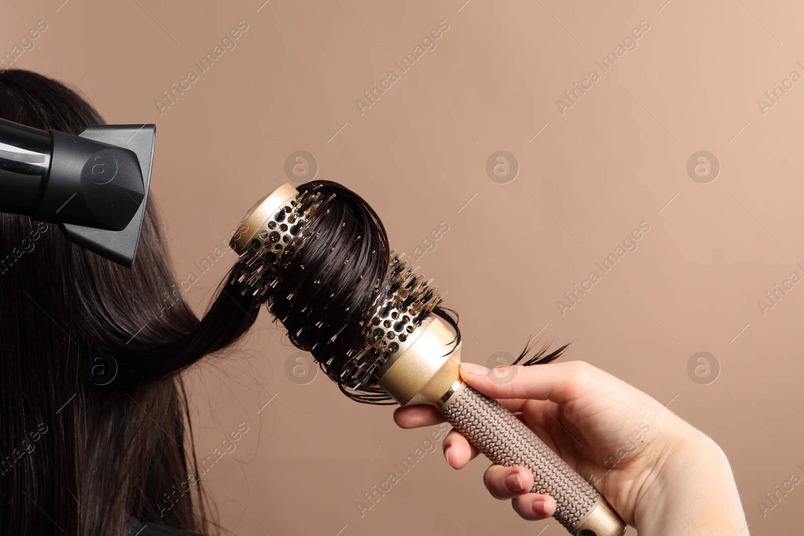 Photo of Hairdresser blow drying client's hair on light brown background, closeup. Space for text