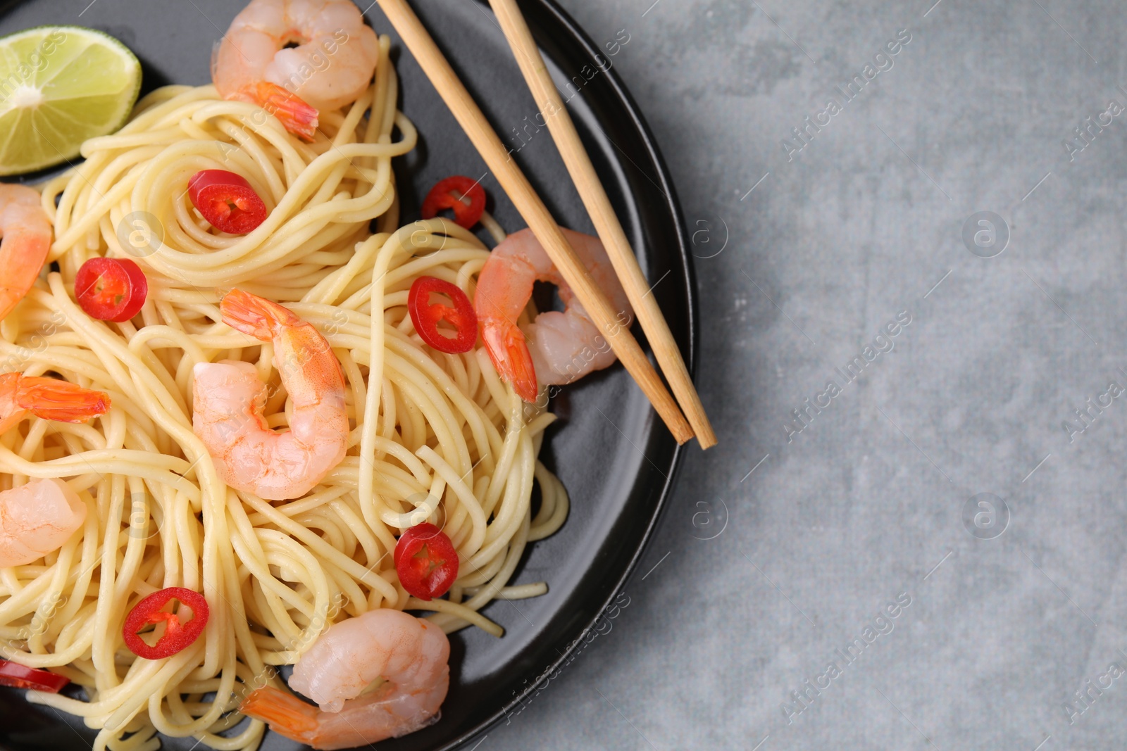 Photo of Tasty spaghetti with shrimps, chili pepper and lime on grey table, top view. Space for text