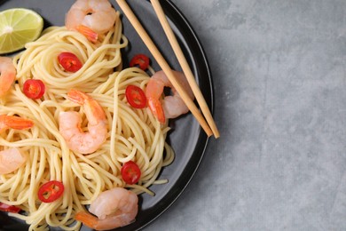 Tasty spaghetti with shrimps, chili pepper and lime on grey table, top view. Space for text