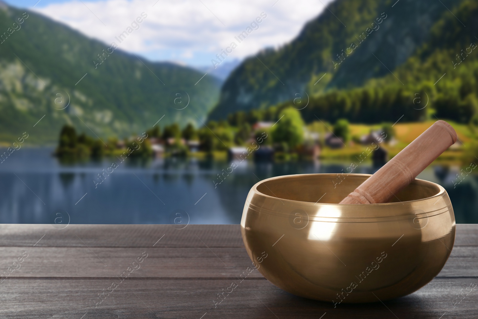 Image of Golden singing bowl and flower on wooden table against mountain landscape. Space for text 