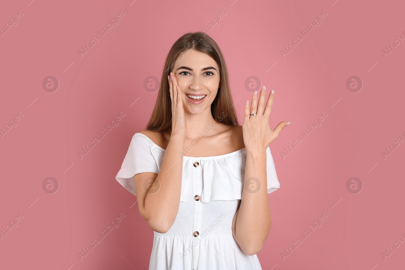 Photo of Happy young woman wearing beautiful engagement ring on pink background