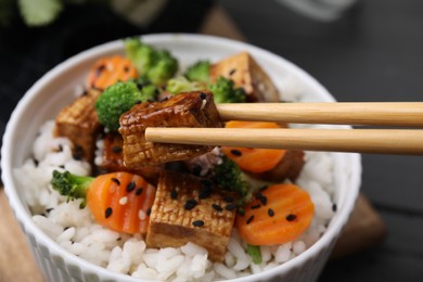 Photo of Taking piece of fried tofu with chopsticks from bowl on table, closeup