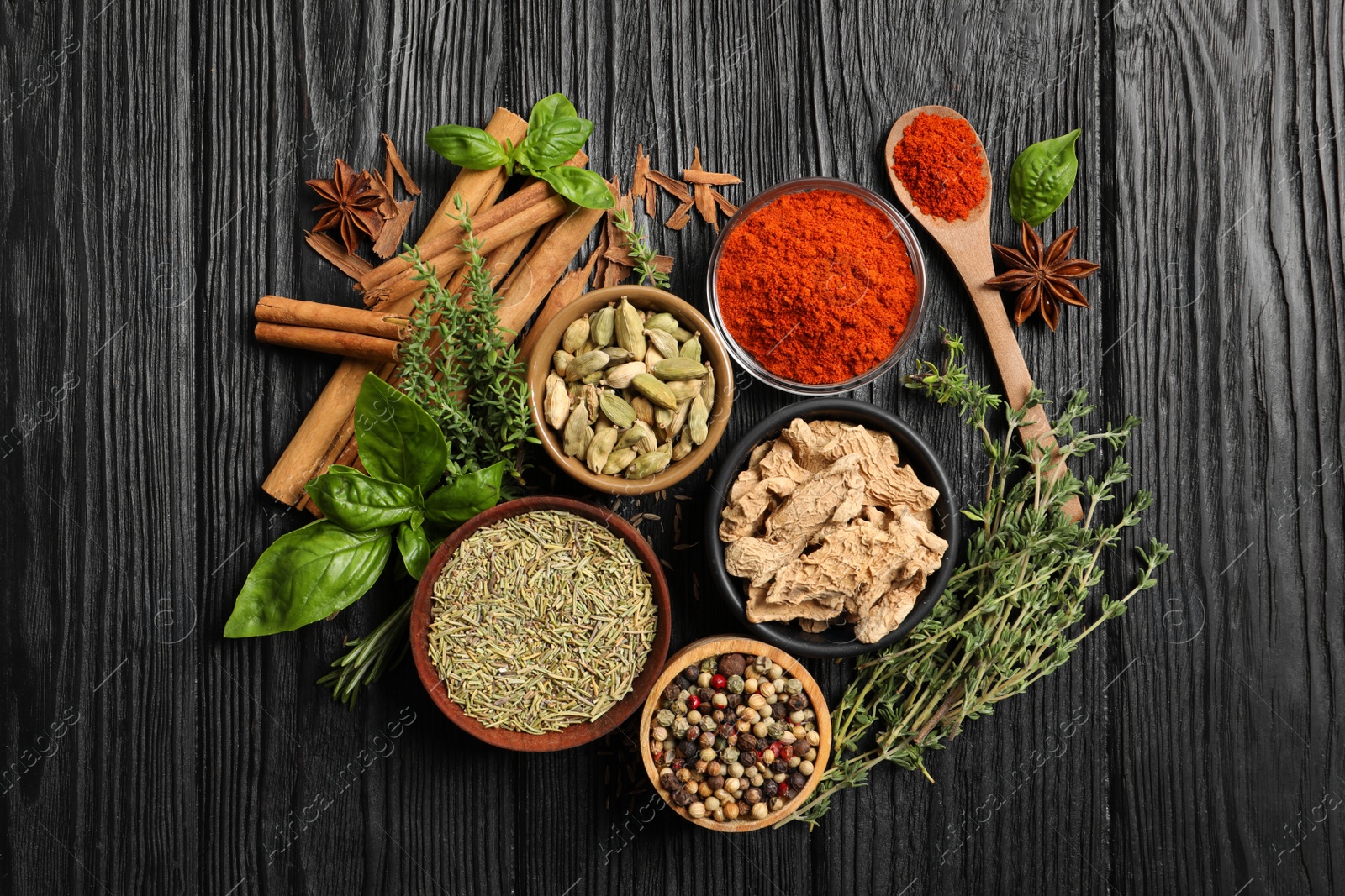Photo of Different natural spices and herbs on black wooden table, flat lay