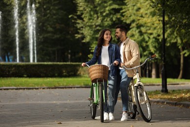 Beautiful couple with bicycles spending time together in park, space for text